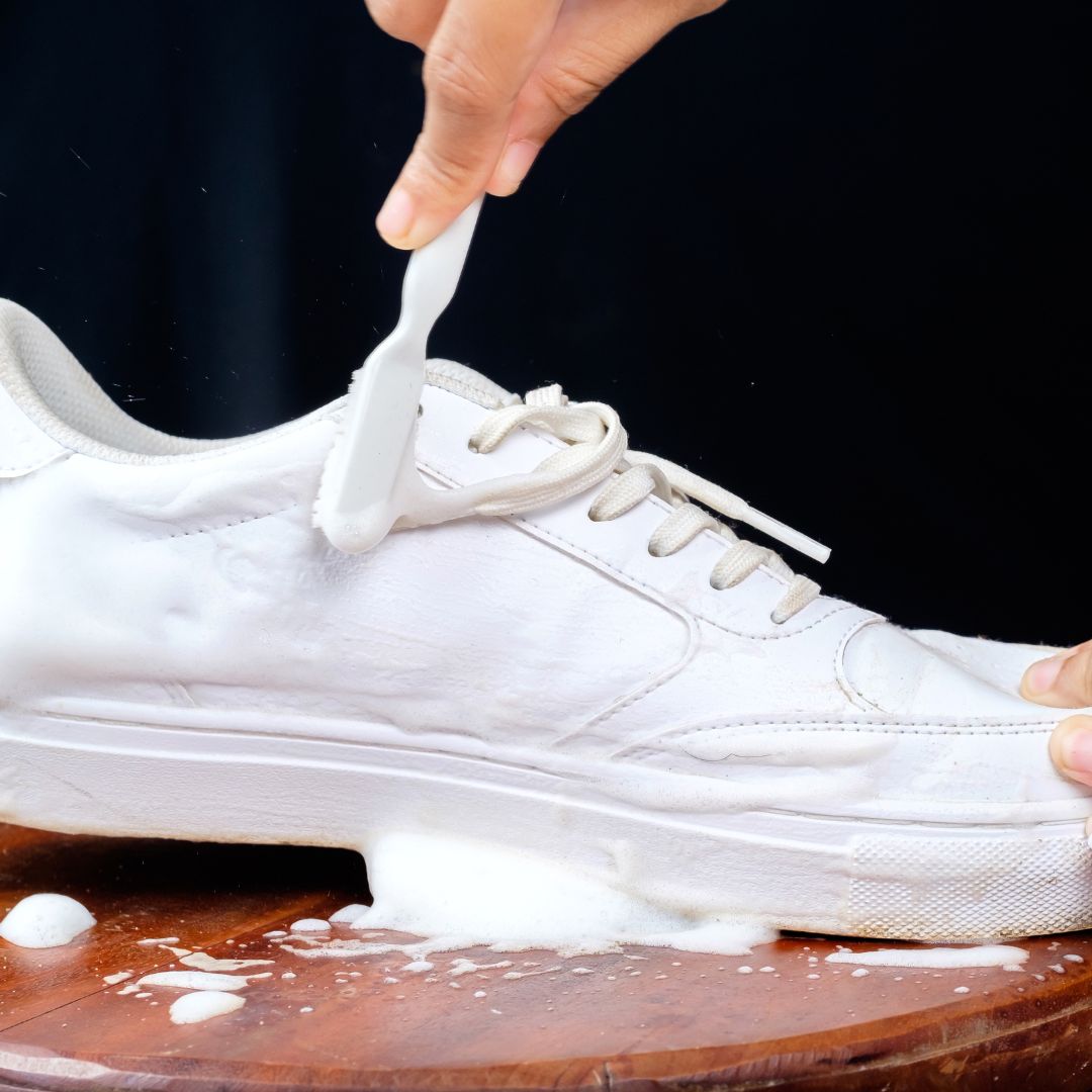 A close up of a white leather shoe being cleaned with a brush.