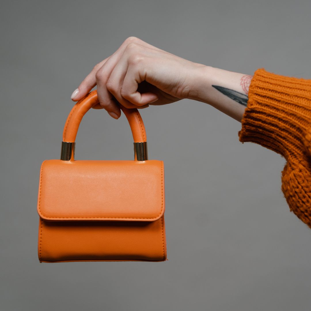 a person's hand holding a small orange leather purse by the handle.